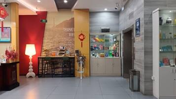 A hotel lobby with a reception desk, a wall-mounted information board, and a seating area.