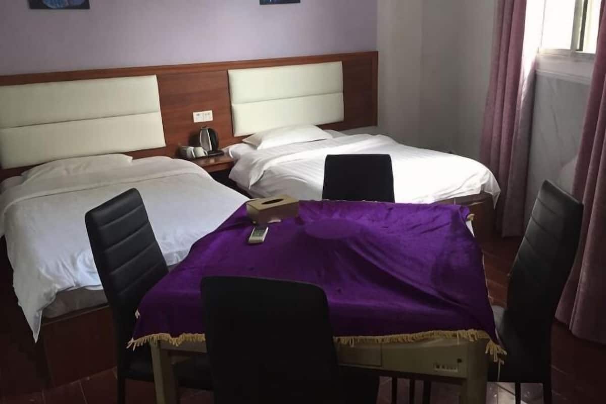 A hotel room with two beds, a table with a purple tablecloth, and a chair.