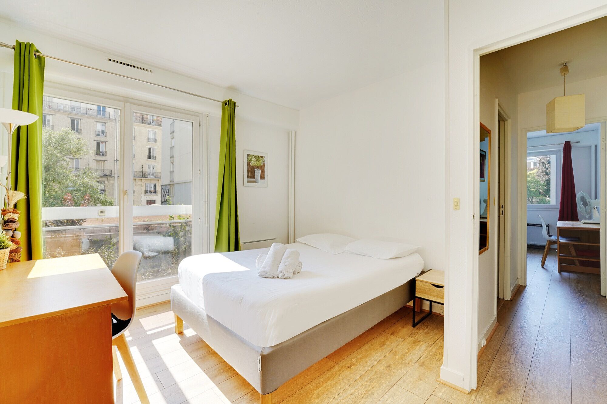 A bedroom with a bed, a desk, and a window with curtains.
