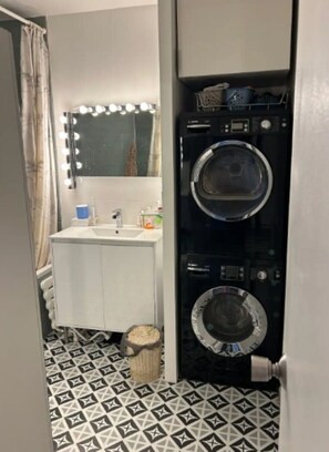 A compact bathroom with a sink, mirror, and two stacked washing machines.