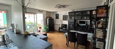 Una cocina moderna con una isla central, una zona de comedor con mesa y sillas, y un espacio de estar con televisión y asientos.