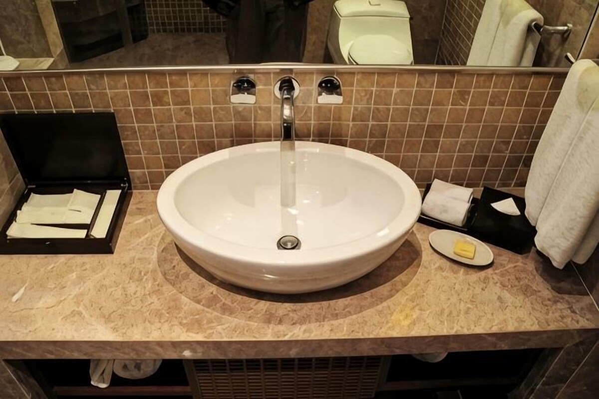 A bathroom with a white sink, mirror, and brown tiled walls.