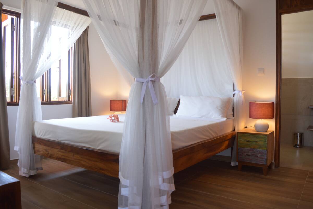 A bedroom with a canopy bed, bedside lamps, and a nightstand with a lamp.