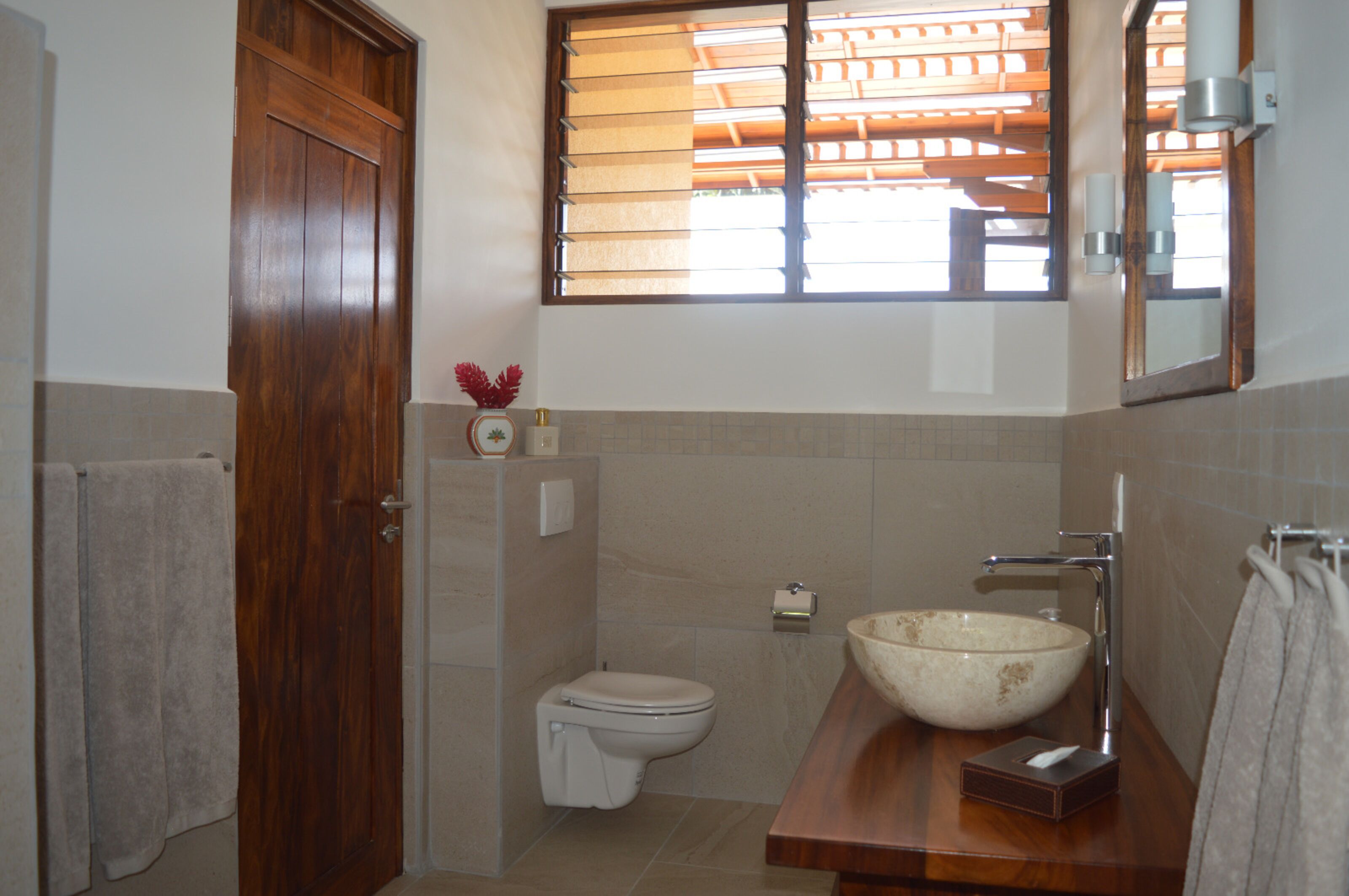 A bathroom with a wooden door, a toilet, a large vessel sink, and a window with blinds.