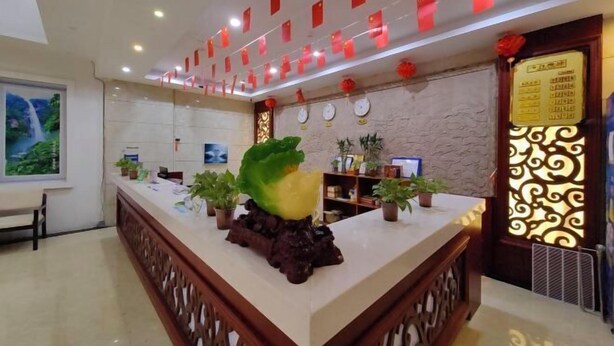 A reception area with a reception desk, potted plants, a wall clock, and a decorative screen. - Yichun Yue Hotel (Yichun)