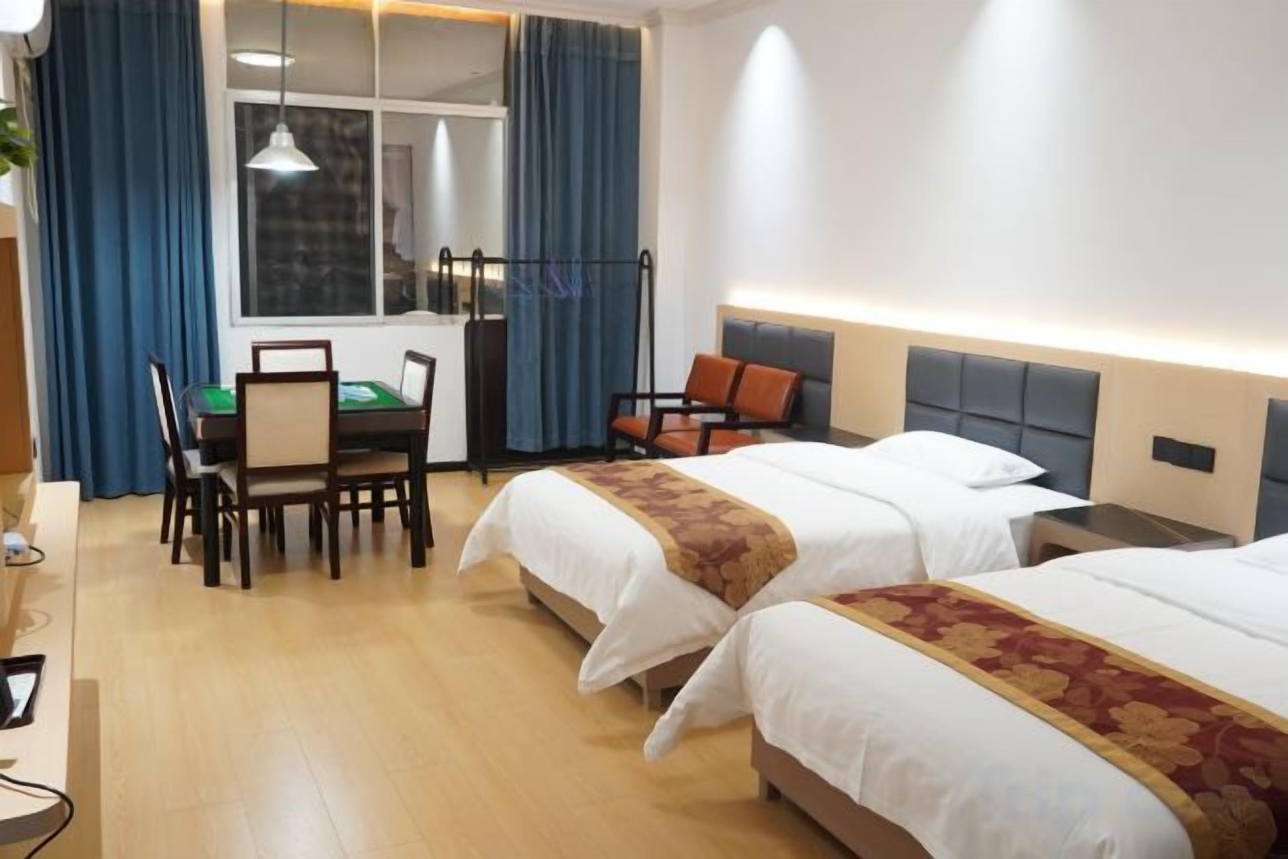 A hotel room with two beds, a desk with a chair, a window with curtains, and a lamp.