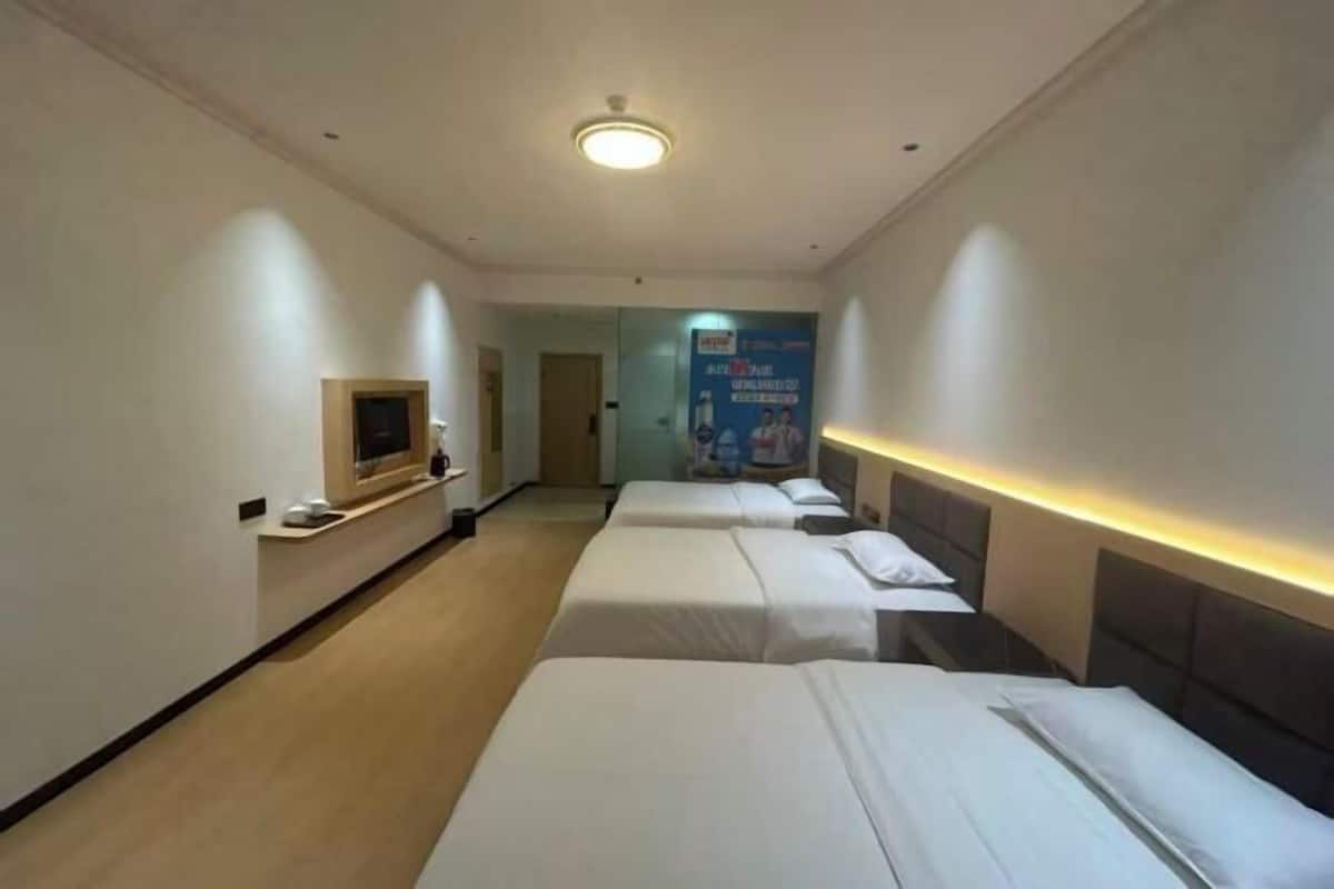 A hotel room with three beds aligned along a corridor, a television on a stand, and a poster on the wall.