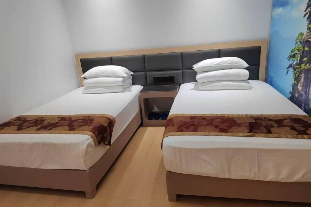 A hotel room with two single beds, a wooden headboard, a small table with a chair, and a mural on the wall.