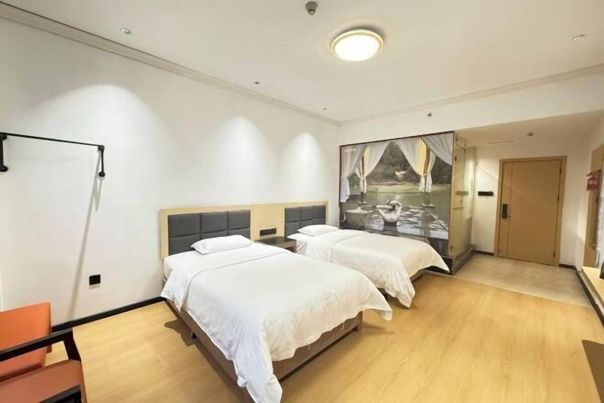 A hotel room with two beds, a wooden floor, and a large window with a view of a garden.