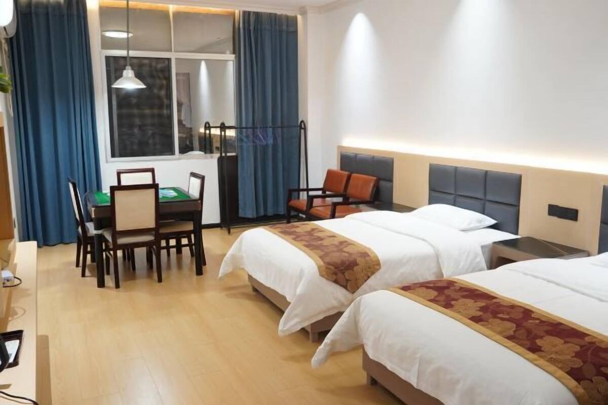A hotel room with two beds, a dining table, chairs, and a window with curtains.