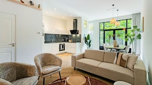 A modern living room with a sofa, armchair, and a dining table with chairs.