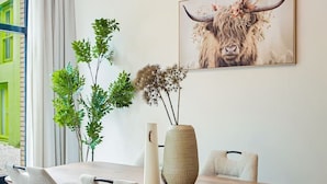 A dining area with a wooden table, four chairs, a vase, and a bull-themed artwork on the wall.