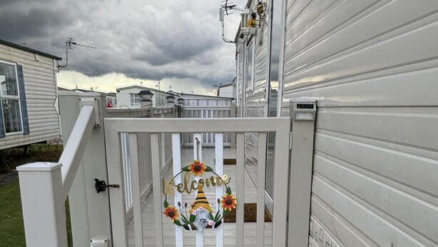Una terraza de madera blanca con un cartel que dice 'Welcome' y una decoración de gnomo.