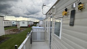 Una casa móvil con fachada blanca, un porche con barandilla blanca y una pequeña terraza.