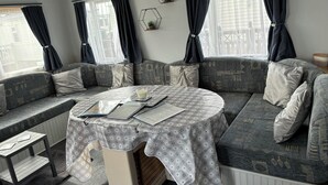 Una habitación acogedora con un sofá modular, una mesita con mantel floreado y una ventana con cortinas oscuras.