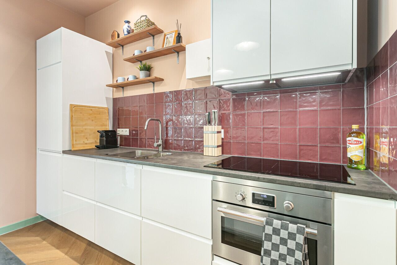 A modern kitchen with white cabinets, a stainless steel oven, a built-in sink, and a red-tiled backsplash.