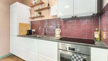 A modern kitchen with white cabinets, a stainless steel oven, a built-in sink, and a red-tiled backsplash.