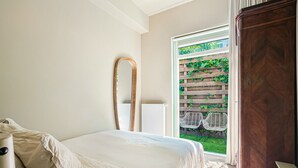 Ein Schlafzimmer mit Bett, einem Holzspiegel, einem Holzschrank und Blick auf einen Garten durch eine Glastür.