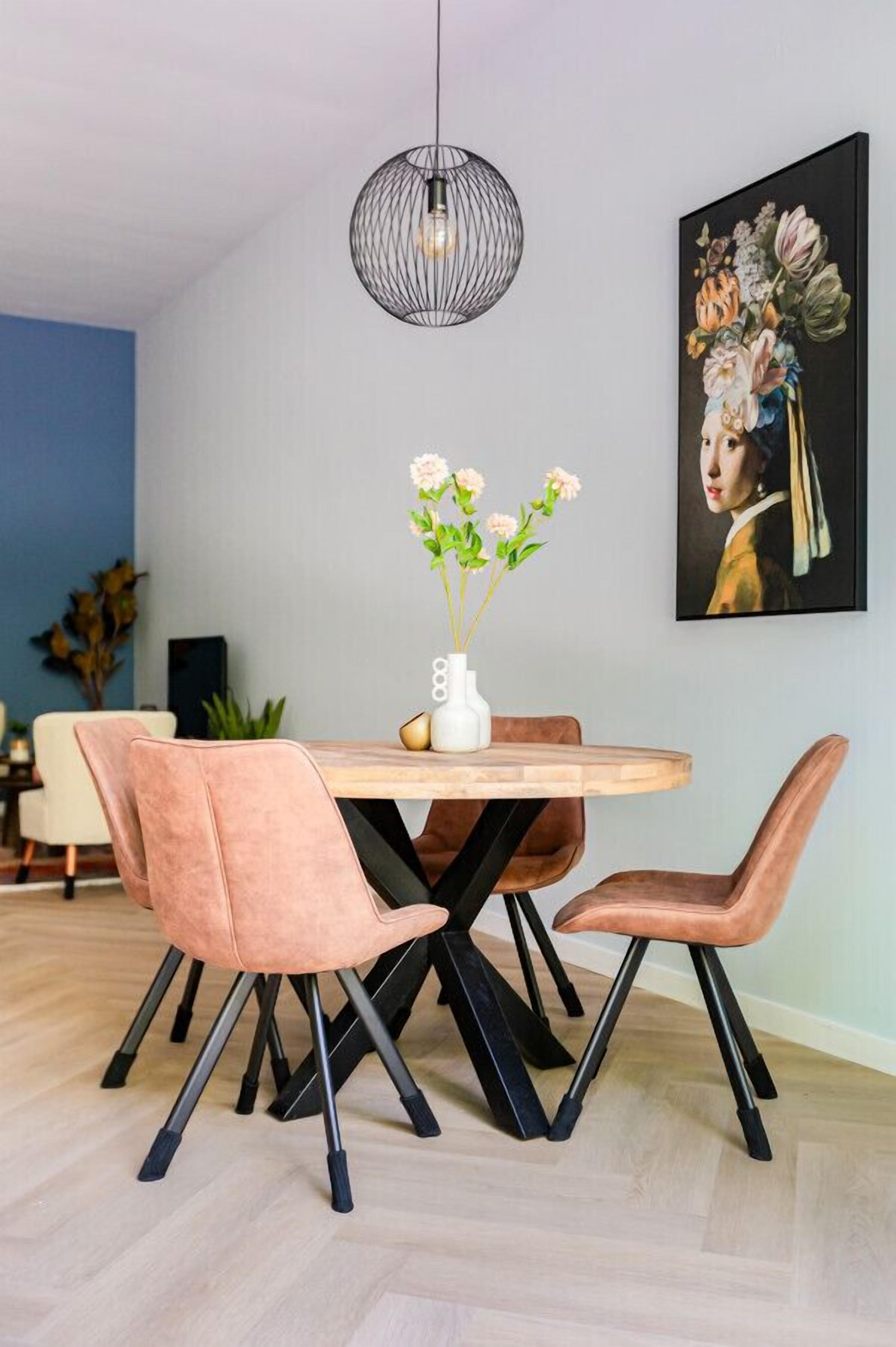 Un coin repas avec une table ronde en bois, quatre chaises rembourrées, un vase blanc orné de fleurs, une suspension noire et un tableau encadré accroché au mur.