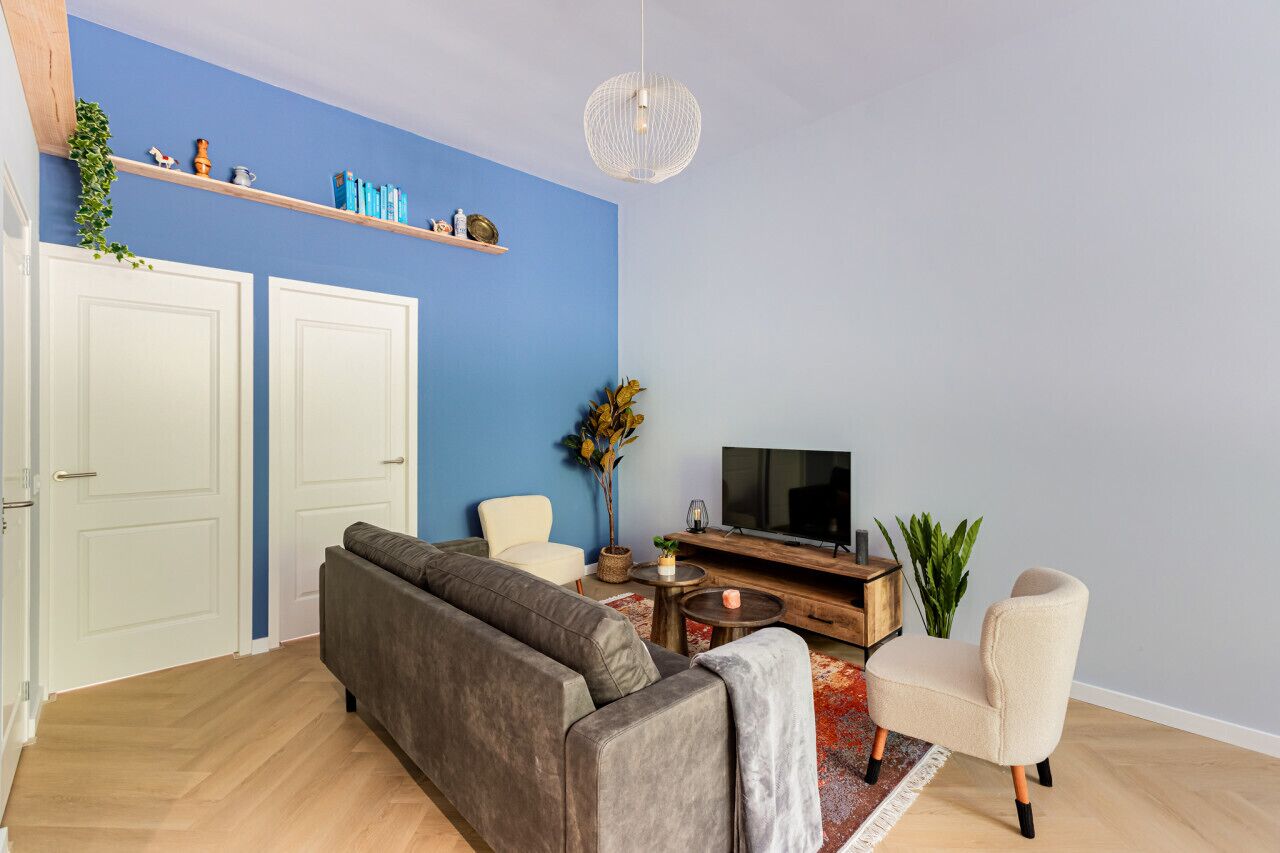 A living room with a sofa, armchairs, a TV, a wooden coffee table, and a plant.