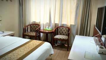 A hotel room with a bed, two chairs, a small table, and a desk with a computer.