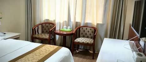 A hotel room with a bed, two chairs, a small table, and a desk with a computer.