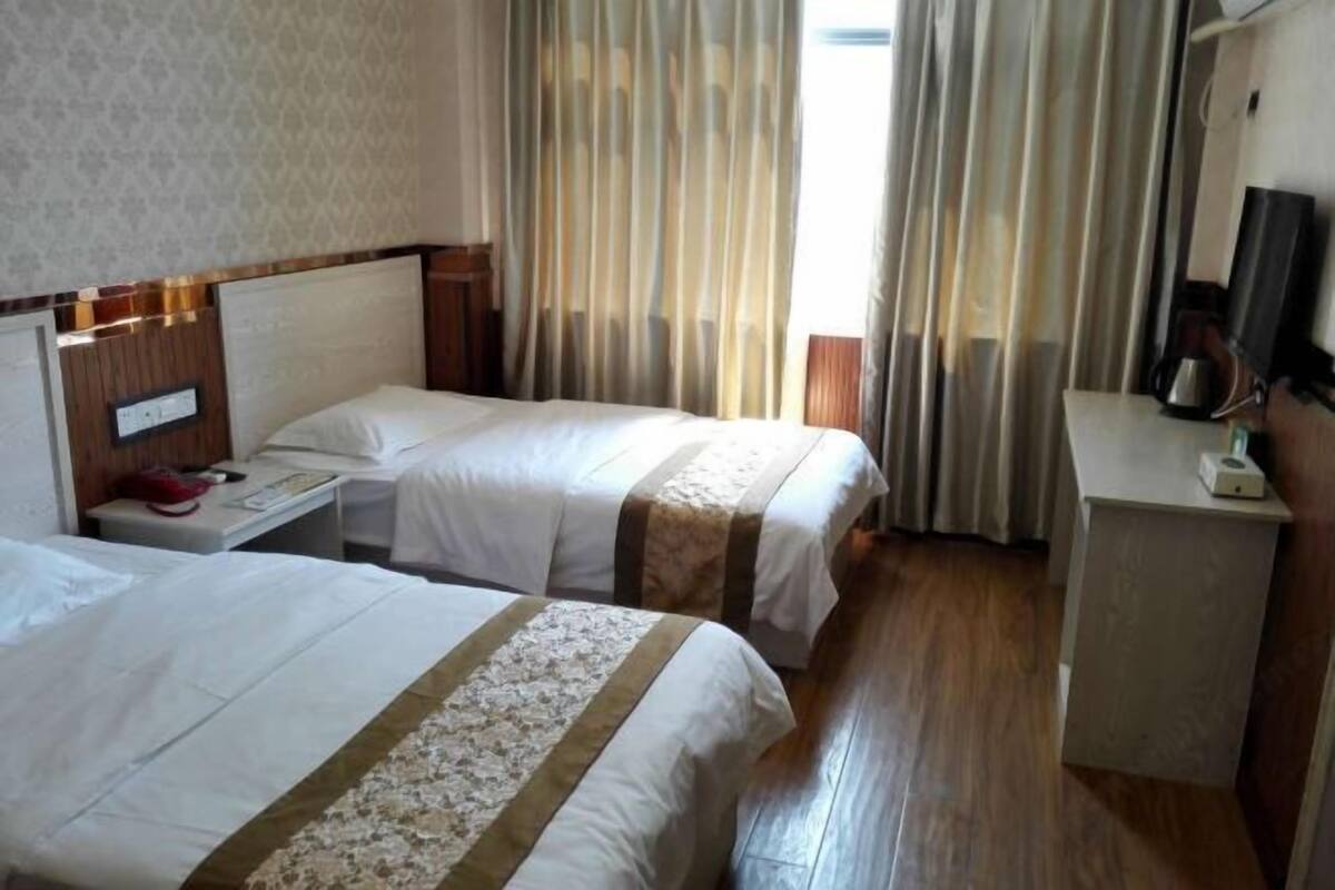 A hotel room with two beds, a desk, a chair, a TV, and a window with curtains.