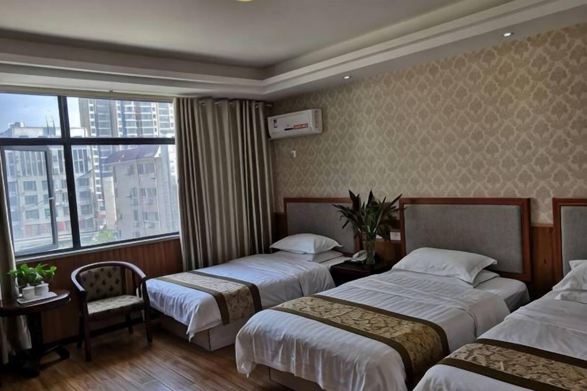 A hotel room with two beds, a desk, a chair, and a large window with curtains.