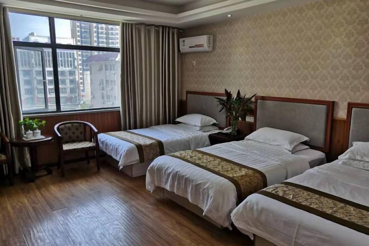 A hotel room with two beds, a chair, a small table, and a potted plant.