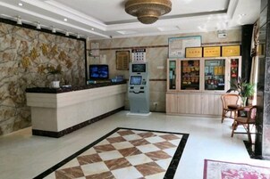 Zona de recepción de hotel con pared de mármol, mostrador de registro, quiosco de autoservicio, refrigerador y escritorio de check-in.