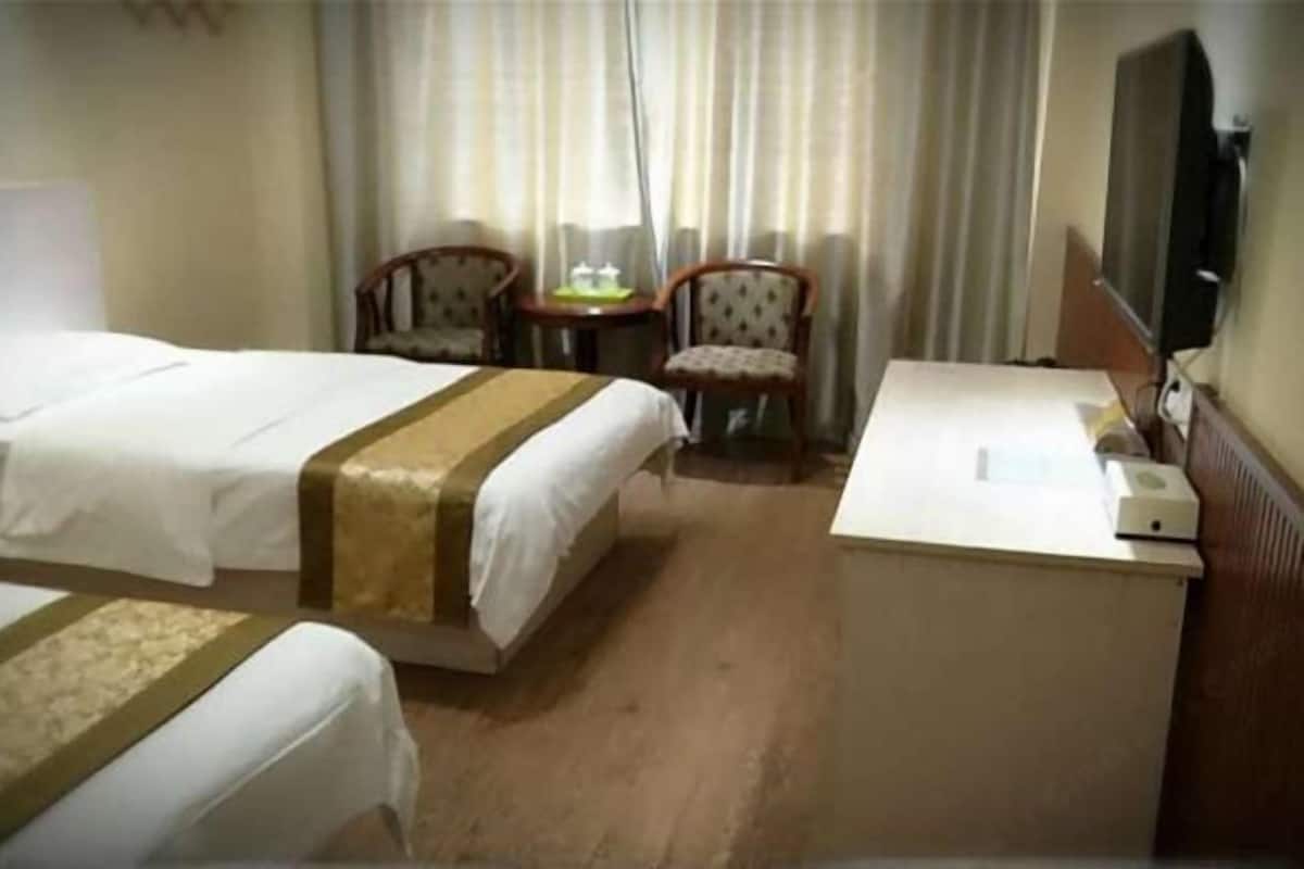 A hotel room with two beds, a desk, a chair, a television, and a window with curtains.