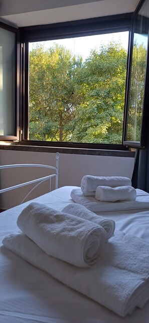 A hotel room with a bed, a window with a view of trees, and a white towel on the bed.