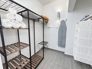 Une salle de bain avec une étagère en métal où sont rangées les serviettes, un rideau de douche suspendu et un porte-serviettes.