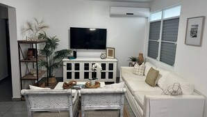 A living room with a white sofa, two wicker chairs, a TV, and a cabinet with decorative items. - Serenity House on Isla Verde Beach (Carolina)