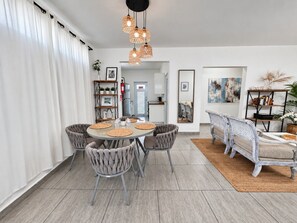 A dining area with a round table, four chairs, and a bench. There is a ceiling light fixture above the table.