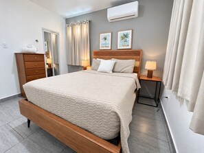 Une chambre à coucher avec un lit en bois, une table de chevet, une commode et un climatiseur fixé au mur.
