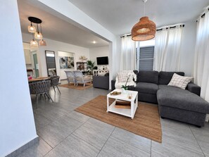 Un salon moderne avec un canapé gris, une table basse blanche et un coin repas comprenant des chaises et une table.