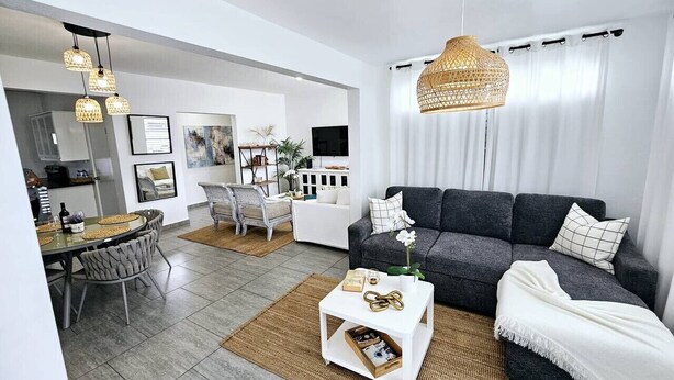 A modern living room with a dark grey sofa, white coffee table, and a dining area with a round table and chairs. - Serenity House on Isla Verde Beach (Carolina)
