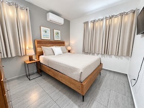 A modern bedroom with a wooden bed, bedside tables, a wall-mounted air conditioner, and curtains.