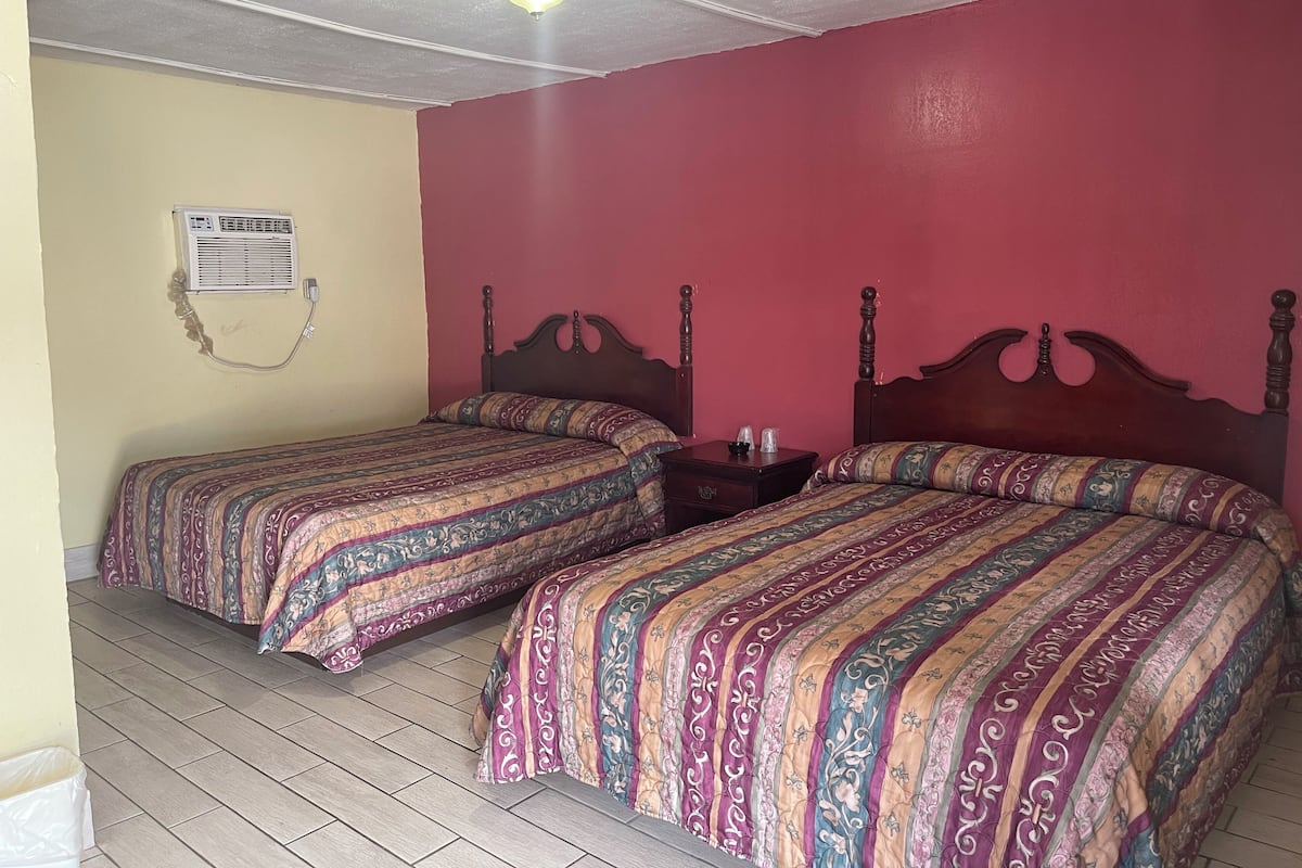A room with two beds, each with patterned bedding, a wooden headboard, and a nightstand with a lamp.