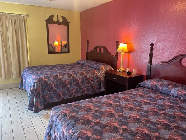 Une chambre d’hôtel avec deux lits, une table de chevet avec une lampe, un miroir et une fenêtre avec des rideaux.