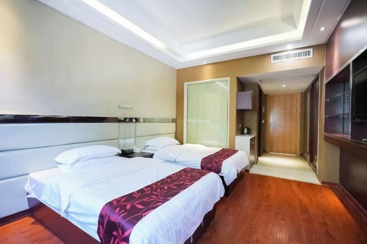 Habitación de hotel con dos camas, un espejo grande, un televisor y suelo de madera.