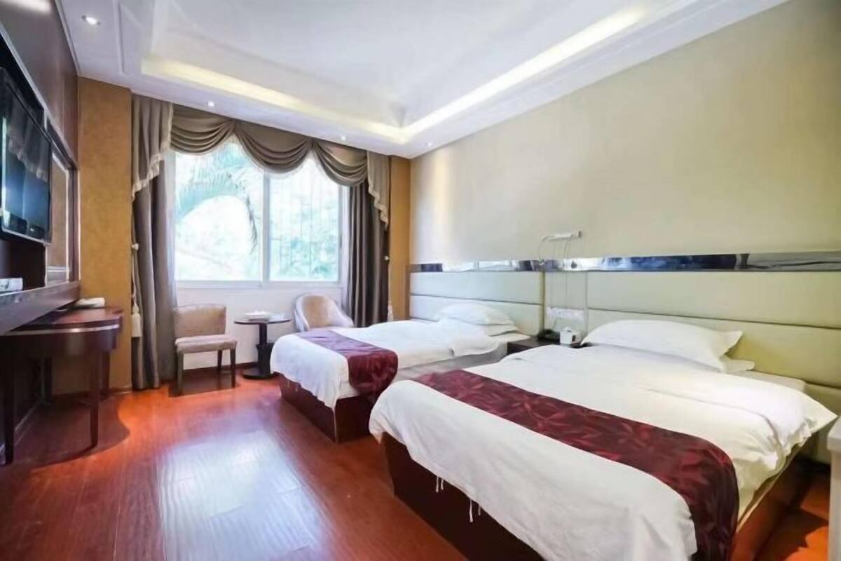 Habitación de hotel con dos camas, televisión, escritorio y ventana con cortinas.