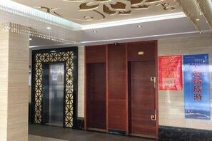 A hotel lobby with a reception desk, a wooden elevator, and a wall with a poster.