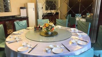 A round table set for dining with a central floral arrangement, surrounded by chairs with green upholstery.