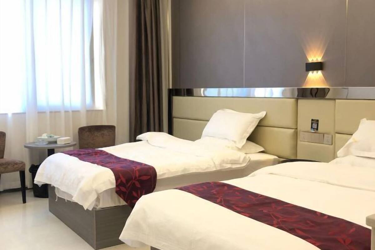 Una habitación de hotel con dos camas, una mesita, una silla y una ventana con cortinas.