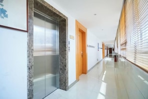 Un pasillo con un ascensor de mármol, una puerta de madera y una ventana con persianas.
