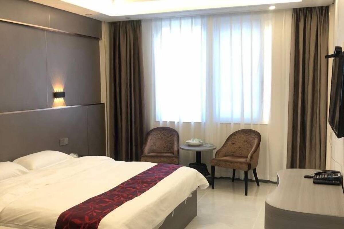 Habitación de hotel con cama, dos sillones, una mesita, un escritorio con teléfono y televisor.