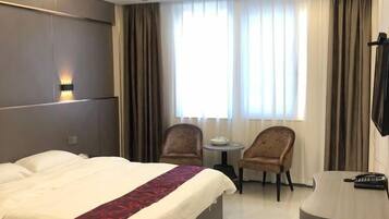A hotel room with a bed, two armchairs, a small table, a desk with a telephone, and a TV.