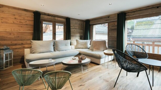 Ein modernes Wohnzimmer mit einer Eckcouch, zwei runden Couchtischen und einer Mischung aus Metall- und Weidekörbchenstühlen.